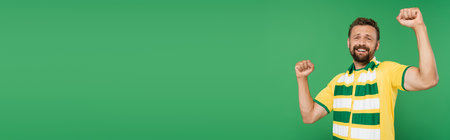 excited sports fan in striped scarf and t-shirt looking at camera isolated on green, bannerの写真素材