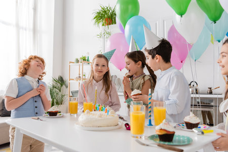 group of joyful children in party caps having fun during birthday party next to colorful balloonsの写真素材