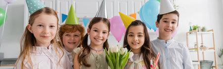 cheerful girl holding tulips near friends during birthday party at home, banner