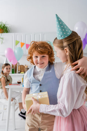 happy redhead boy hugging girl with present during birthday partyの写真素材