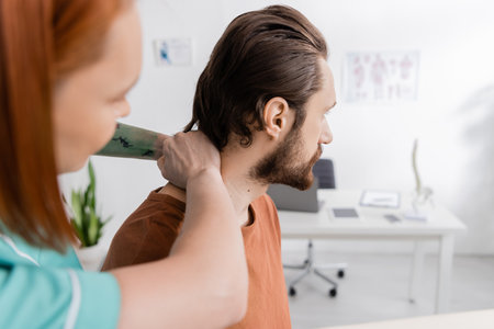 blurred physiotherapist examining neck of injured man during appointment in rehabilitation centerの写真素材