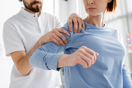 partial view of chiropractor examining painful shoulder of woman in consulting roomの写真素材