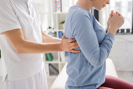 cropped view of physiotherapist examining injured back of woman in consulting roomの写真素材