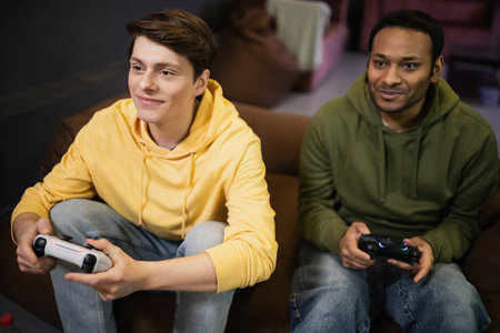 KYIV, UKRAINE - FEBRUARY 13, 2023: Pleased man playing video game with indian friend in gaming clubの写真素材
