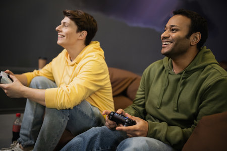 Smiling indian man playing video game near blurred friend in gaming clubの写真素材