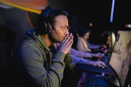 Concentrated indian man in headphones looking at computer monitor in gaming clubの写真素材