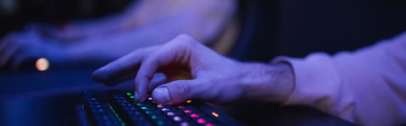 Cropped view of player using keyboard with lighting in cyber club, banner
