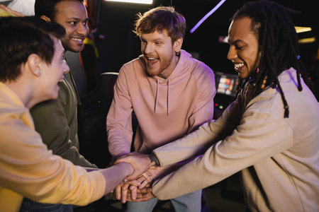 Cheerful multiethnic friends holding hands while spending time in gaming club