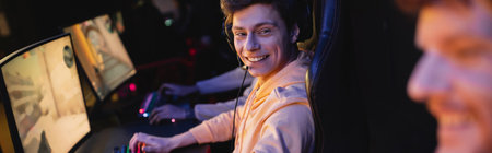 Smiling gamer in headset looking at blurred friend in gaming blub, banner