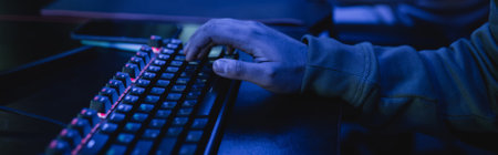 Cropped view of gamer using keyboard in gaming club with blue lighting, banner