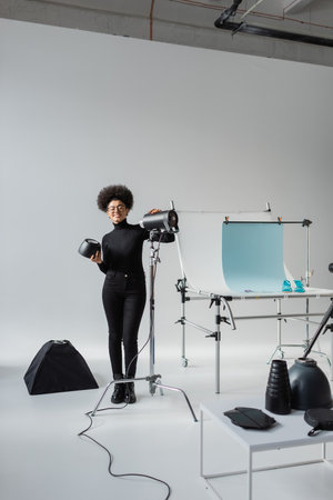 full length of happy african american content maker near strobe lamp and shooting table in contemporary photo studioの写真素材