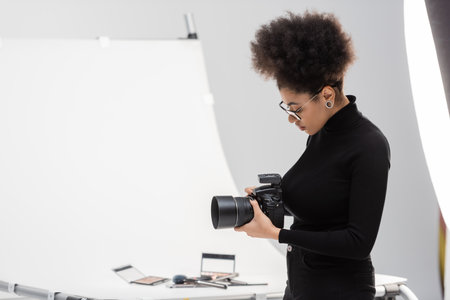side view of african american photographer with digital camera near shooting table with decorative...