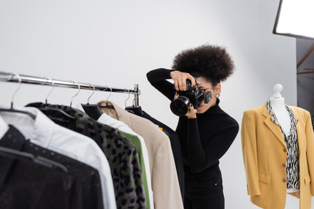 african american photographer taking picture of fashionable clothes collection on rail rack in photo studioの写真素材