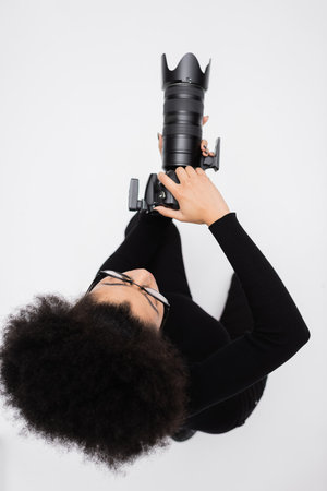 top view of african american photographer in black clothes taking photo on digital camera isolated on greyの写真素材