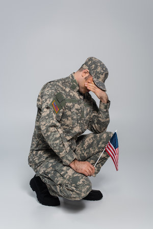 army soldier crying and covering face while holding flag of United States during memorial day on greyの写真素材