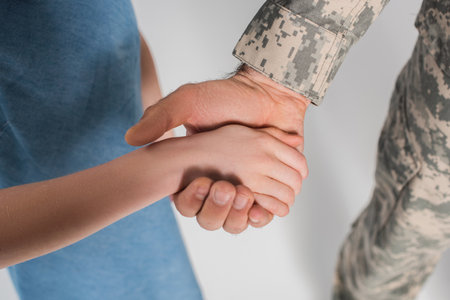 cropped view of preteen girl holding hand of brave father in army uniform during memorial day isolated on greyの写真素材
