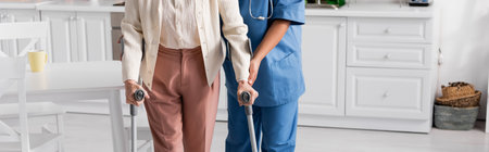 cropped view of senior woman using crutches while walking near nurse at home, banner