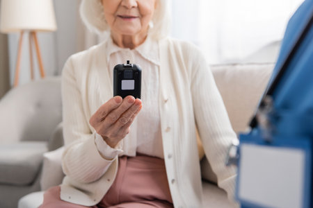 cropped view of happy senior woman holding glucometer near nurse in blue uniformの写真素材