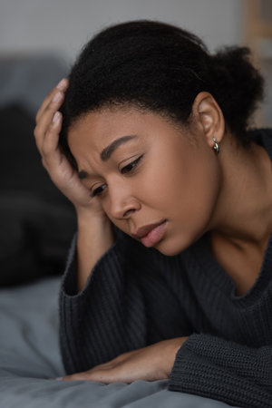 Portrait of upset multiracial woman lying on blurred bed at home