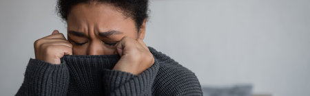 Depressed multiracial woman in knitted sweater crying at home, bannerの写真素材