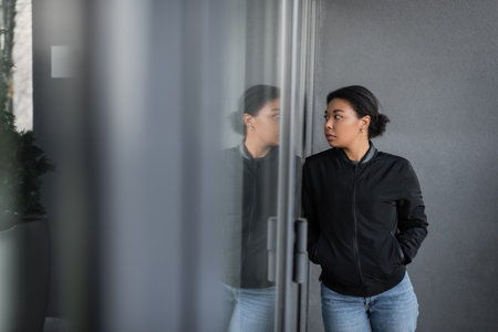 multiracial woman with depression looking at glass on door of building outdoorsの写真素材