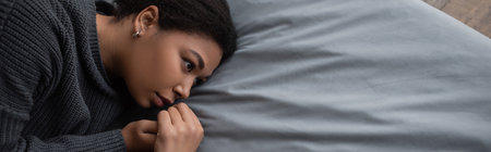 Top view of depressed multiracial woman with apathy looking away on bed, banner