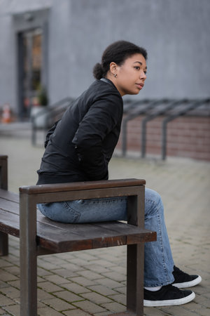 multiracial woman with mental crisis sitting on bench on urban streetの写真素材