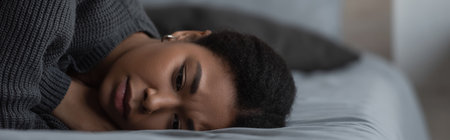 Frustrated multiracial woman with depression lying on blurred bed at home, bannerの写真素材