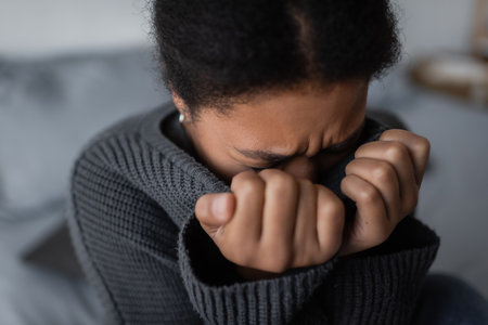 Sad multiracial woman in sweater crying in blurred bedroom at homeの写真素材