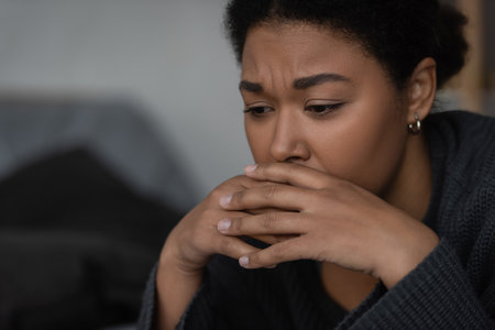 Displeased multiracial woman in sweater having apathy and looking away at homeの写真素材