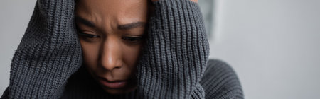 Worried multiracial woman in sweater touching head at home, bannerの写真素材