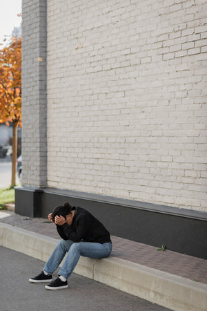 Depressed multiracial woman sitting on border near building outdoorsの写真素材