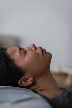 Side view of heartbroken multiracial woman crying on pillow at homeの写真素材