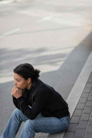 Young multiracial woman with depression looking away while sitting on border outdoorsの写真素材
