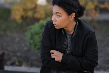 Young multiracial woman with depression sitting outdoors in autumnの写真素材