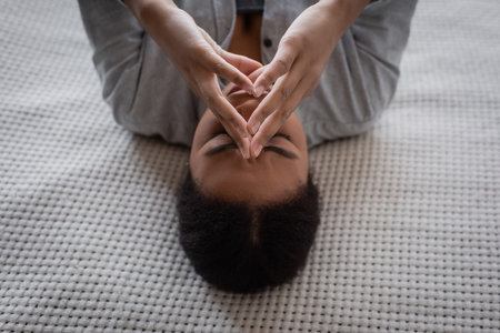 High angle view of sad multiracial woman with depression lying on bed at homeの写真素材