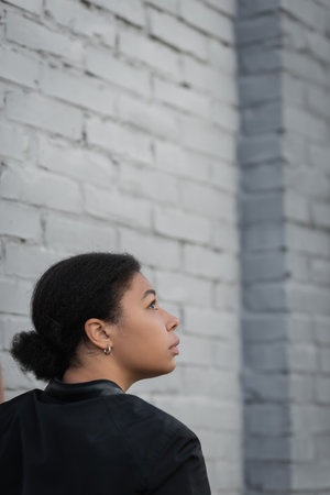 Side view of multiracial woman with psychological problem standing near brick wallの写真素材