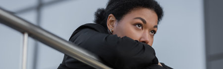 Young multiracial woman with apathy and depression standing near railing on urban street, bannerの写真素材