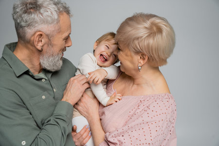 excited toddler girl laughing near happy grandparents isolated on greyの写真素材