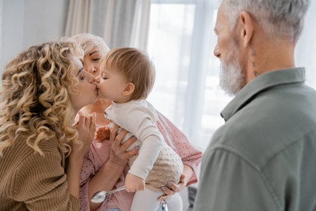 blonde woman kissing beloved daughter near mature parents at homeの写真素材