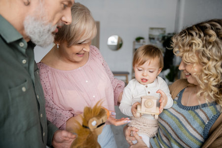 little child looking at toy car near happy grandparents and mother in living room