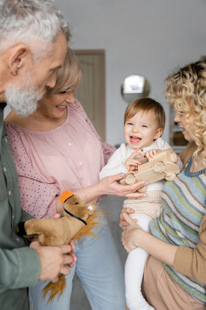 baby girl holding toy car and laughing near mom and grandparents at home