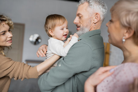 displeased girl crying in hands of bearded grandfather at homeの写真素材