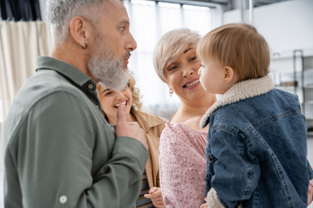 funny bearded man grimacing near little granddaughter and cheerful family at homeの写真素材