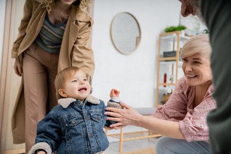 little girl in denim jacket smiling near mother and happy granny while meeting at homeの写真素材