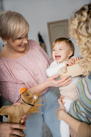 carefree child holding toy car and laughing near grandparents and mother in living roomの写真素材