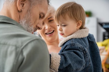 happy middle aged woman smiling near toddler granddaughter and husband at homeの写真素材
