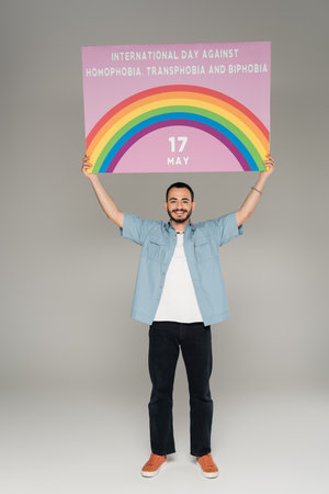 Carefree gay man holding placard with International Day Against Homophobia, Transphobia and Biphobia...