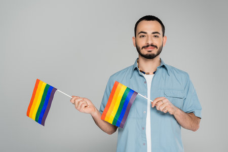 Portrait of bearded gay man holding lgbt flags isolated on grey, International Day Against Homophobiaの写真素材