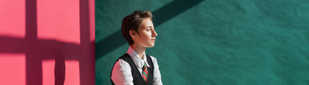 stylish young woman with short hair posing in school uniform on green and pink background with...